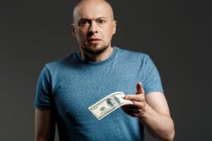 A distressed man holding out a hundred-dollar bill.