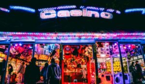A casino entrance at night with people standing, illuminated by neon lights.