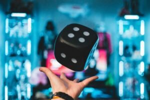 A person tosses a large black die with white dots, captured mid-air.
