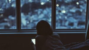 A person lies on a bed, focused on her phone.